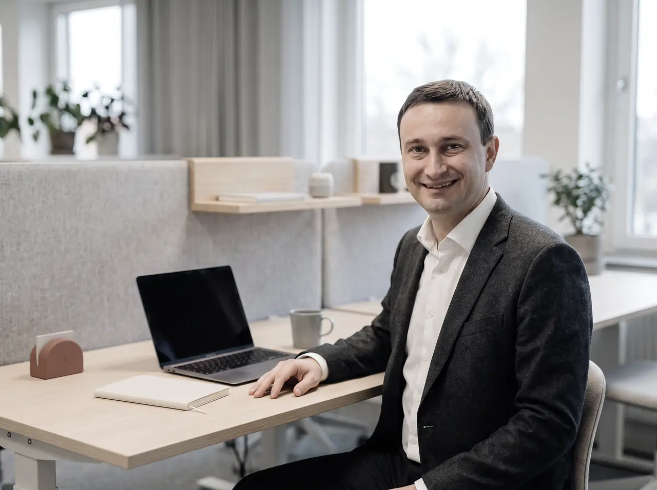 Stefan Franz an einem Schreibtisch in einem hellen, modernen Büro, daneben ein aufgeklappter Laptop und ein Notizbuch.