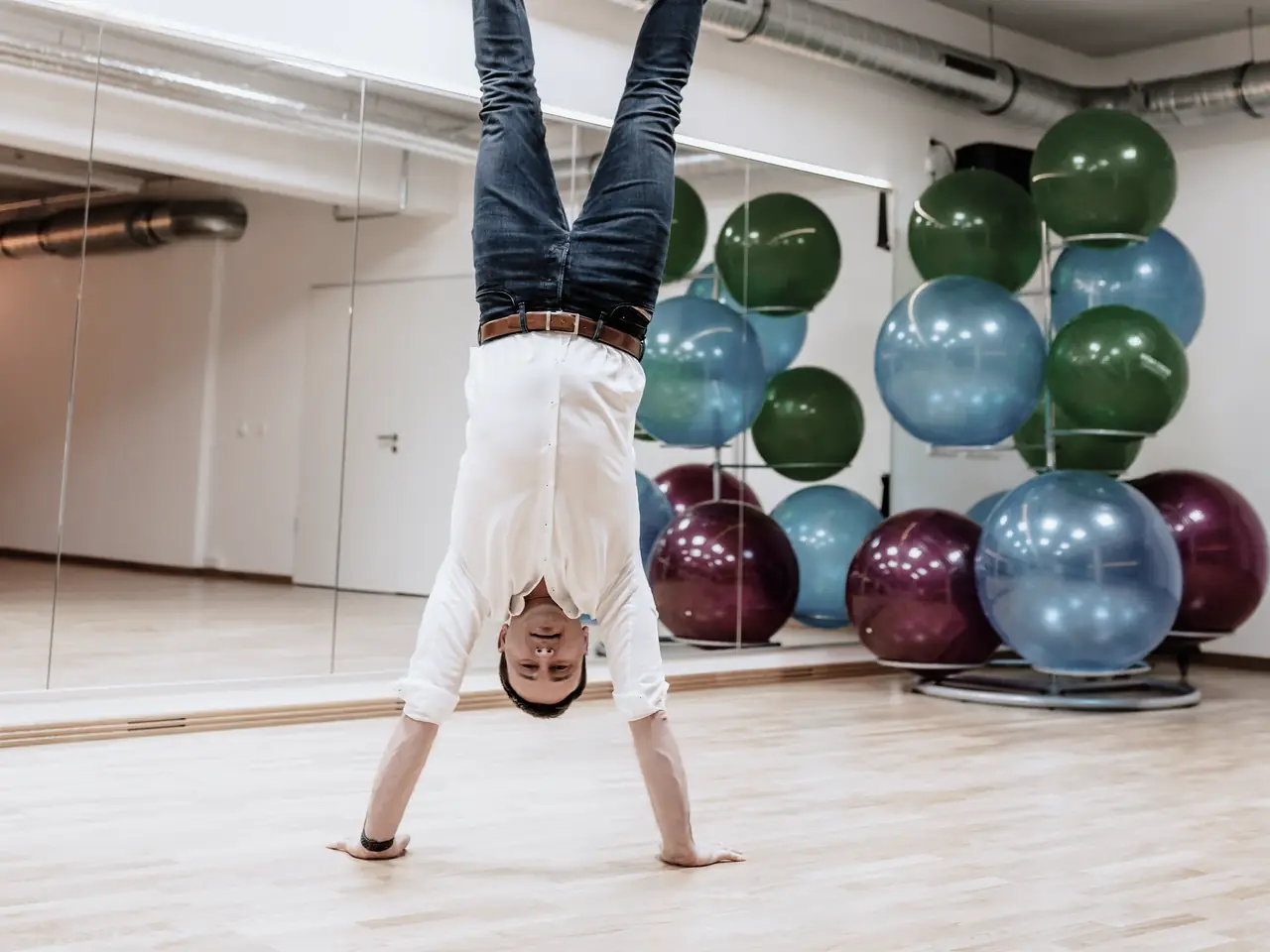 Stefan Franz macht in einer Turnhalle einen Handstand, im Hintergrund ein Ständer mit Gymnastikbällen.